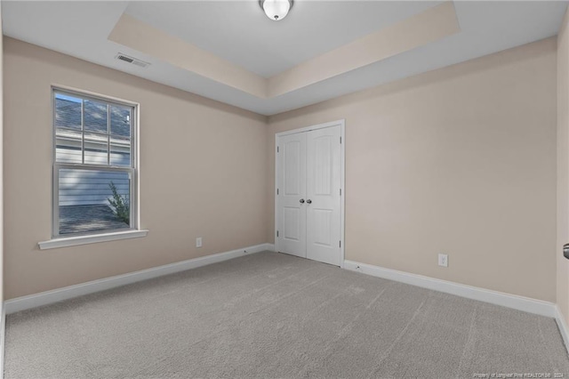 spare room featuring light carpet and a tray ceiling