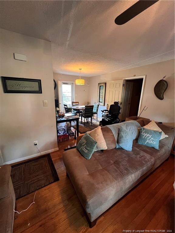 living room with ceiling fan, dark hardwood / wood-style floors, and a textured ceiling