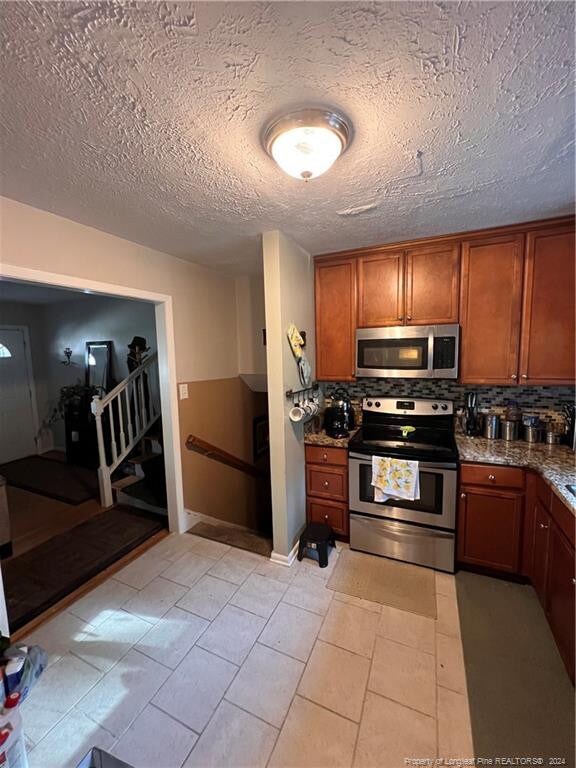 kitchen with decorative backsplash, stone counters, stainless steel appliances, light tile patterned floors, and a textured ceiling