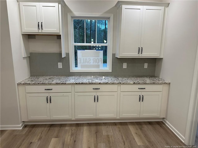 kitchen with white cabinetry, decorative backsplash, light stone countertops, and light wood-type flooring