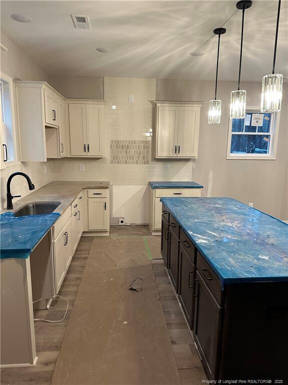 kitchen featuring sink, dark stone countertops, white cabinets, backsplash, and hanging light fixtures