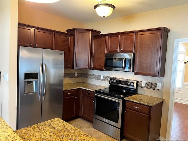 kitchen with light stone counters, tasteful backsplash, appliances with stainless steel finishes, and light wood-type flooring