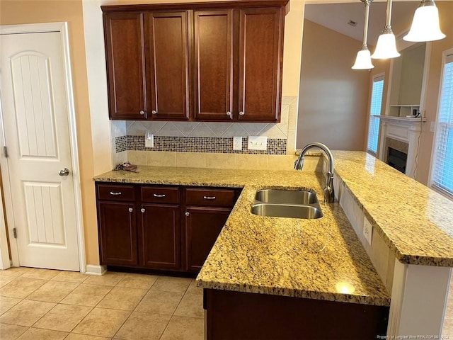 kitchen with kitchen peninsula, backsplash, sink, light stone countertops, and decorative light fixtures