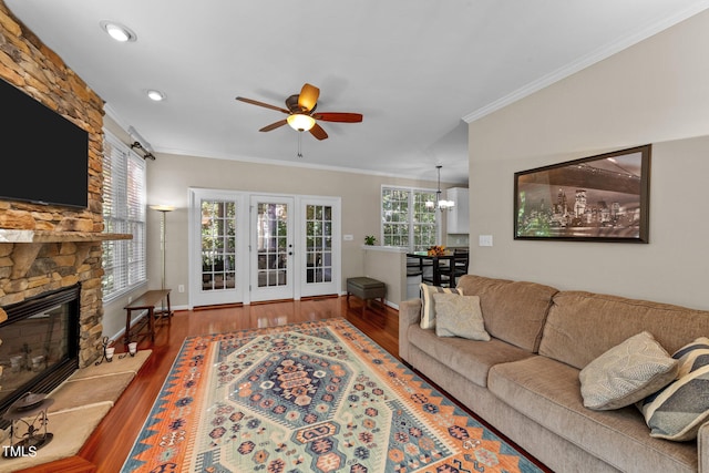 living room featuring crown molding, a fireplace, wood-type flooring, and ceiling fan with notable chandelier