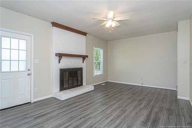 unfurnished living room featuring a fireplace, dark hardwood / wood-style flooring, a textured ceiling, and a healthy amount of sunlight