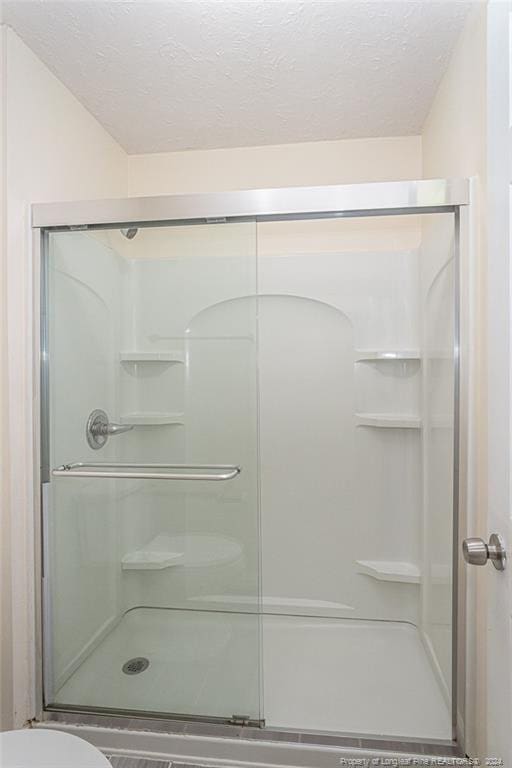 bathroom with an enclosed shower, a textured ceiling, and toilet