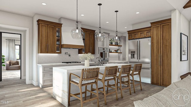 kitchen with decorative light fixtures, refrigerator with ice dispenser, backsplash, a kitchen island with sink, and light hardwood / wood-style flooring