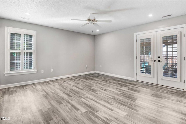 empty room with french doors, plenty of natural light, light hardwood / wood-style flooring, and a textured ceiling