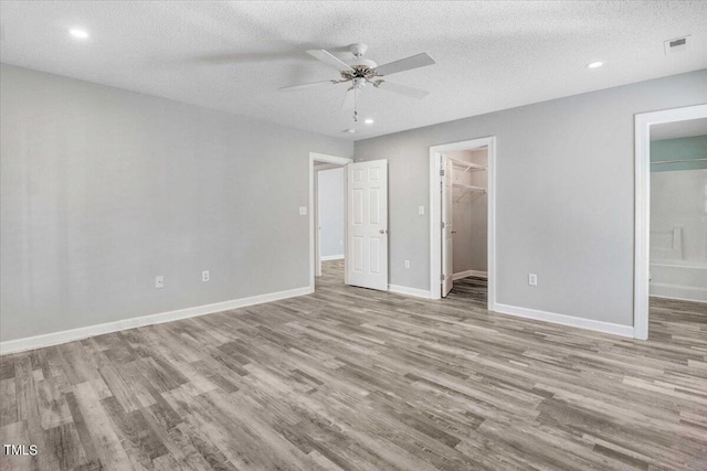 unfurnished bedroom featuring connected bathroom, a spacious closet, light hardwood / wood-style flooring, a textured ceiling, and a closet