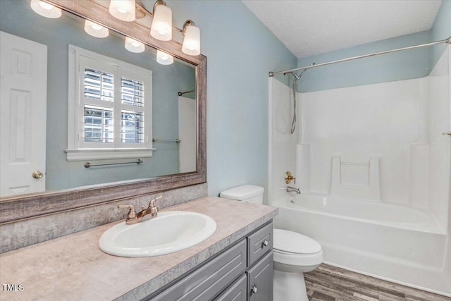 full bathroom featuring toilet,  shower combination, wood-type flooring, a textured ceiling, and vanity