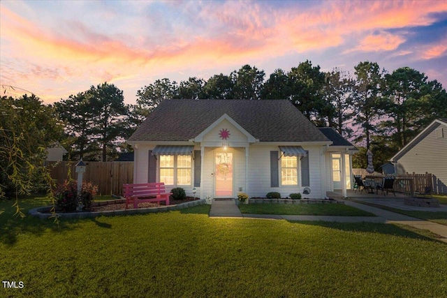 view of front of home featuring roof with shingles, fence, and a front yard