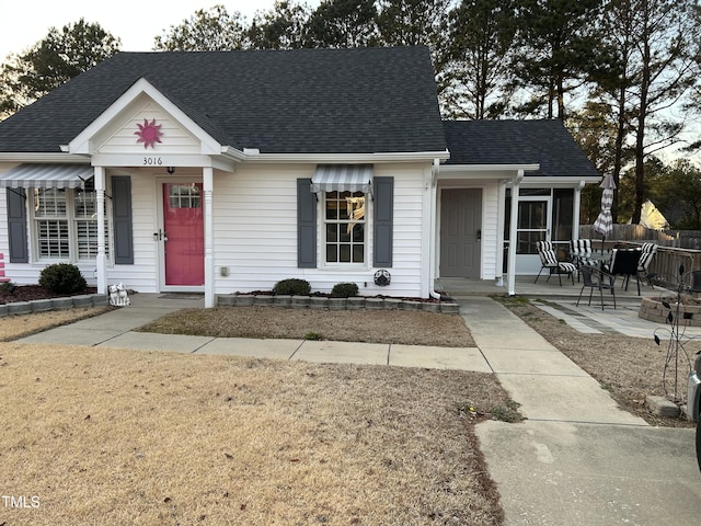 view of front of property featuring a patio area, a shingled roof, and fence