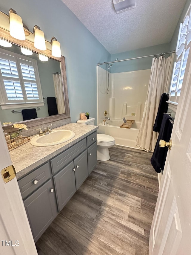 bathroom with a textured ceiling, toilet, wood finished floors, vanity, and shower / bath combo