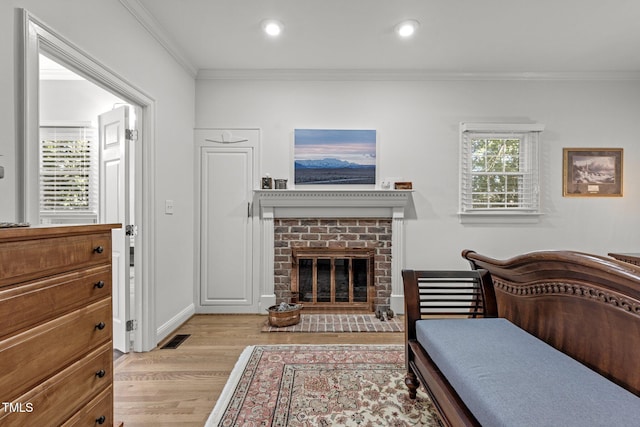 bedroom with a brick fireplace, ornamental molding, light hardwood / wood-style flooring, and multiple windows