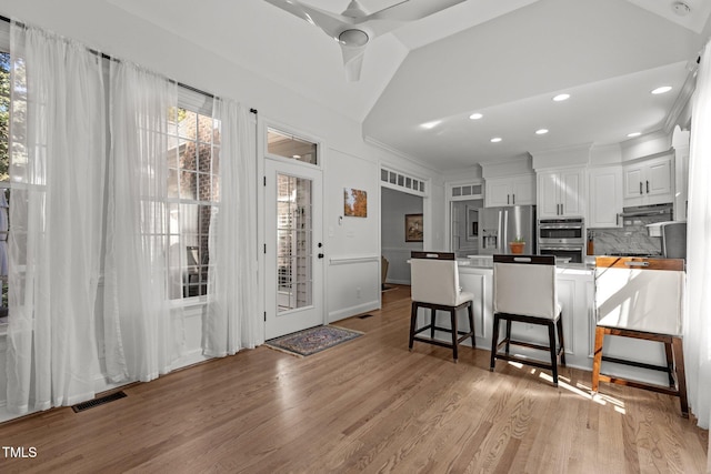 kitchen featuring a kitchen breakfast bar, stainless steel appliances, kitchen peninsula, lofted ceiling, and white cabinetry