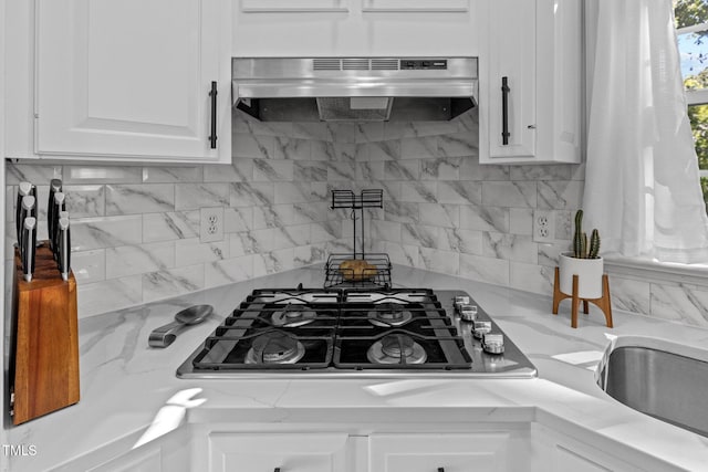 kitchen with white cabinets, tasteful backsplash, stainless steel gas stovetop, exhaust hood, and light stone countertops