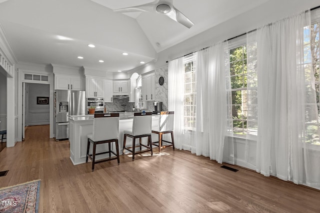 kitchen featuring kitchen peninsula, light hardwood / wood-style flooring, white cabinetry, appliances with stainless steel finishes, and a kitchen bar