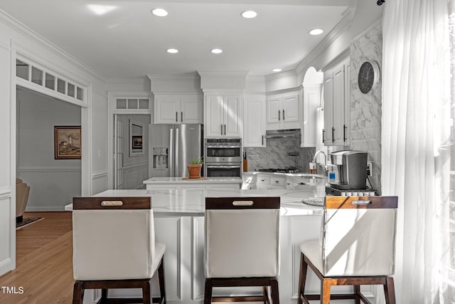 kitchen with kitchen peninsula, white cabinetry, hardwood / wood-style flooring, appliances with stainless steel finishes, and a kitchen bar