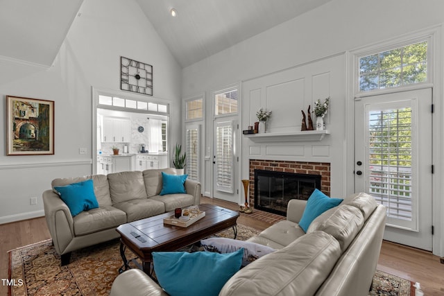 living room with a brick fireplace, high vaulted ceiling, and light hardwood / wood-style flooring