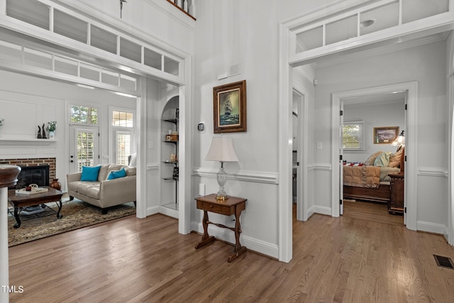 foyer featuring wood-type flooring, a brick fireplace, and a towering ceiling