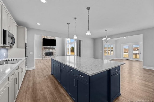 kitchen with pendant lighting, blue cabinets, white cabinets, black electric stovetop, and light stone countertops