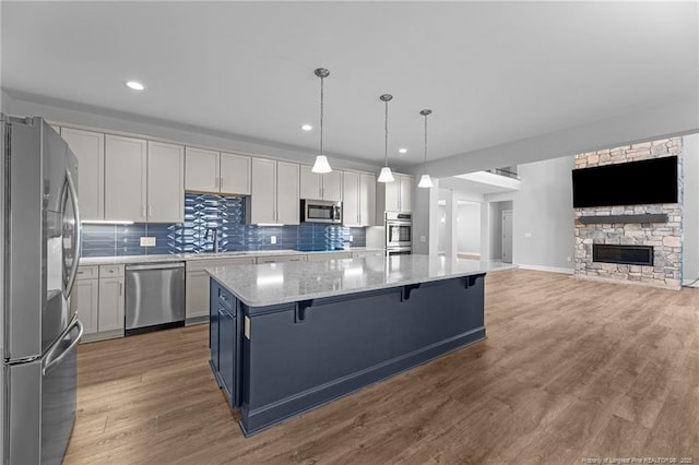 kitchen featuring decorative light fixtures, a kitchen bar, a center island, stainless steel appliances, and light stone countertops