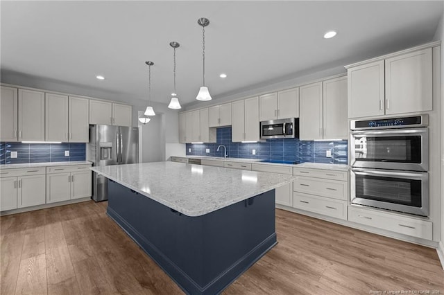 kitchen with white cabinetry, hanging light fixtures, appliances with stainless steel finishes, a kitchen island, and hardwood / wood-style floors