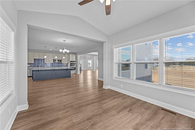 unfurnished living room with dark wood-type flooring, lofted ceiling, and ceiling fan with notable chandelier