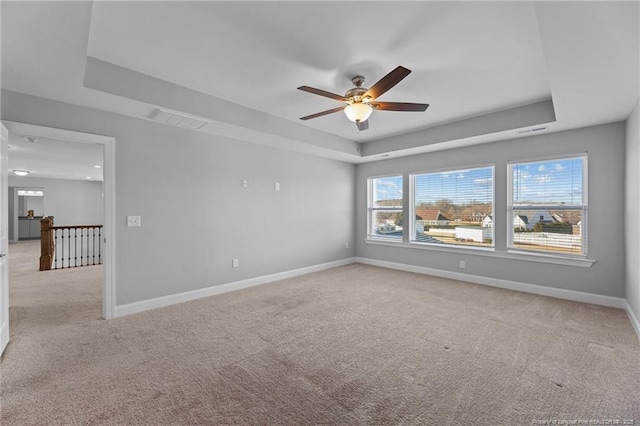 spare room featuring ceiling fan, a tray ceiling, and light carpet