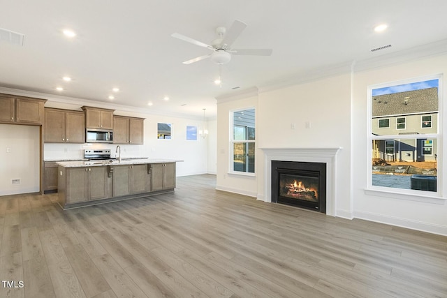 kitchen with appliances with stainless steel finishes, light wood-type flooring, a kitchen island with sink, and crown molding