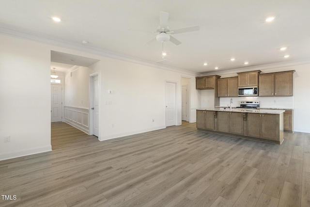 kitchen featuring ornamental molding, stainless steel appliances, light hardwood / wood-style floors, and a kitchen island with sink