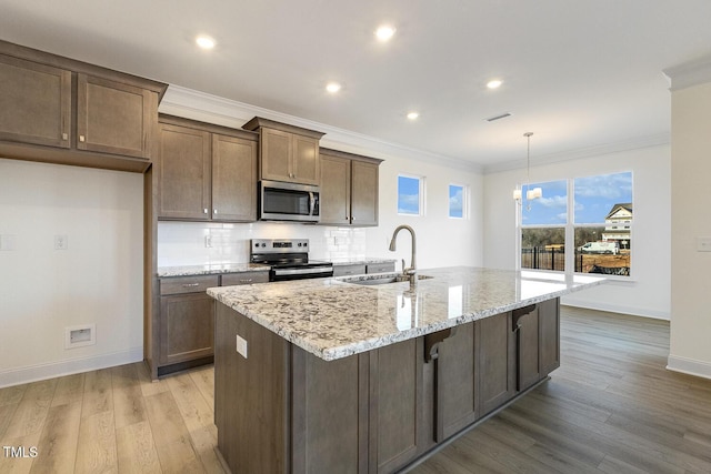 kitchen featuring stainless steel appliances, sink, light stone counters, an island with sink, and pendant lighting