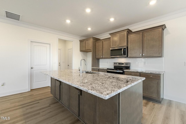 kitchen featuring light stone countertops, a center island with sink, light wood-type flooring, appliances with stainless steel finishes, and sink