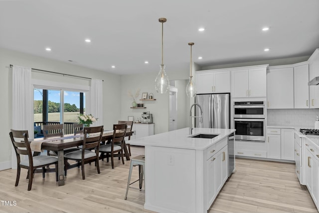 kitchen with stainless steel appliances, light countertops, light wood-type flooring, tasteful backsplash, and an island with sink