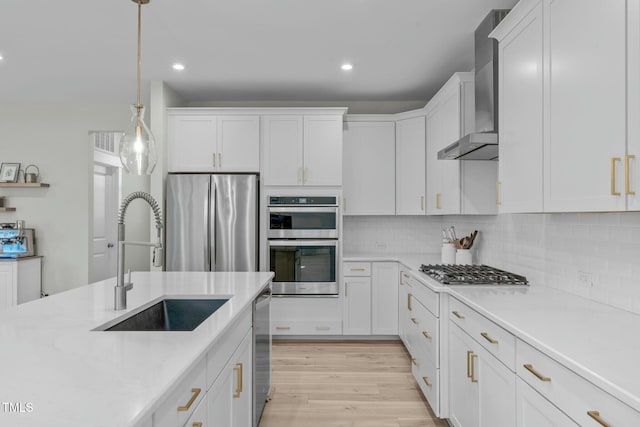 kitchen with stainless steel appliances, a sink, white cabinets, light countertops, and wall chimney range hood