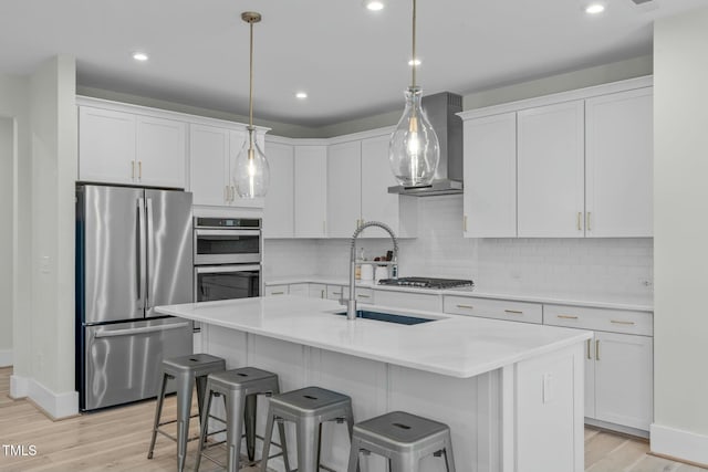 kitchen featuring light wood finished floors, wall chimney exhaust hood, appliances with stainless steel finishes, and white cabinets