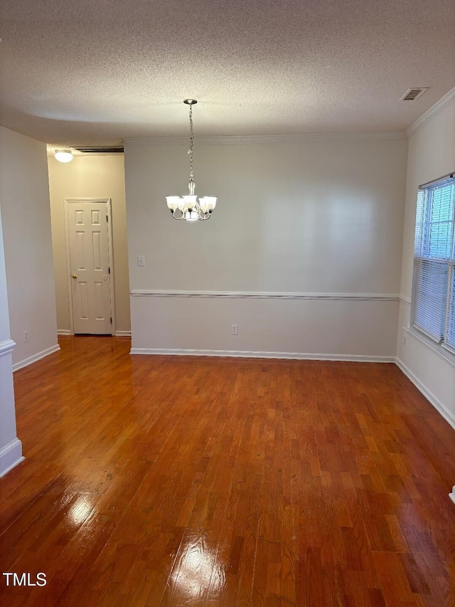 empty room featuring a textured ceiling, ornamental molding, hardwood / wood-style flooring, and a chandelier