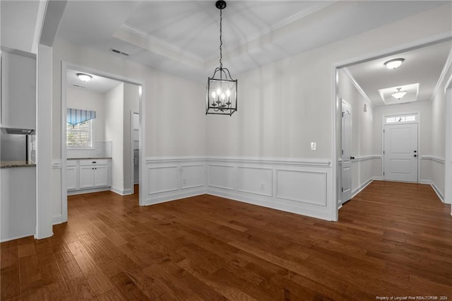 unfurnished dining area featuring dark wood-type flooring, ornamental molding, and an inviting chandelier