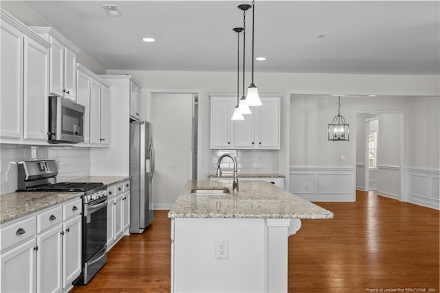 kitchen with stainless steel appliances, sink, white cabinetry, a center island with sink, and decorative light fixtures