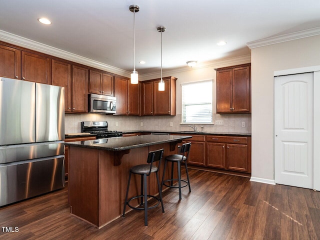 kitchen featuring pendant lighting, ornamental molding, appliances with stainless steel finishes, a center island, and dark hardwood / wood-style flooring