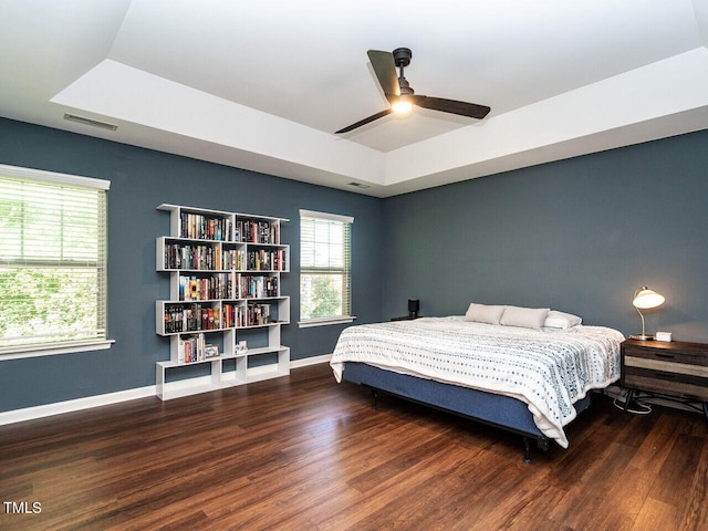 bedroom with ceiling fan, a tray ceiling, and dark wood-type flooring