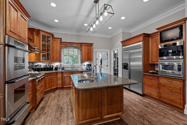 kitchen with appliances with stainless steel finishes, an island with sink, hanging light fixtures, crown molding, and hardwood / wood-style flooring