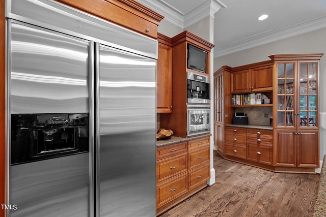 kitchen with dark stone countertops, crown molding, stainless steel appliances, and hardwood / wood-style floors