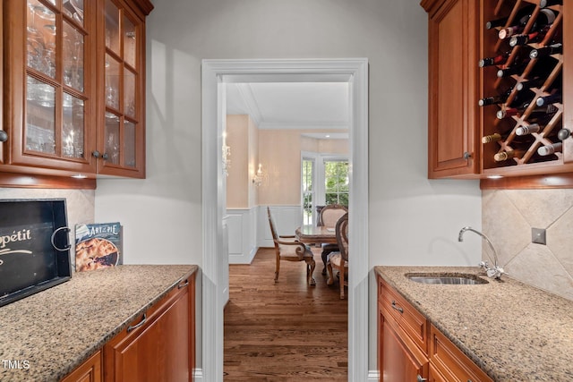 bar featuring tasteful backsplash, light stone countertops, sink, ornamental molding, and dark hardwood / wood-style floors