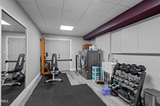 exercise room with a drop ceiling, light hardwood / wood-style floors, and separate washer and dryer