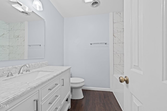 bathroom featuring hardwood / wood-style floors, toilet, tiled shower, and vanity