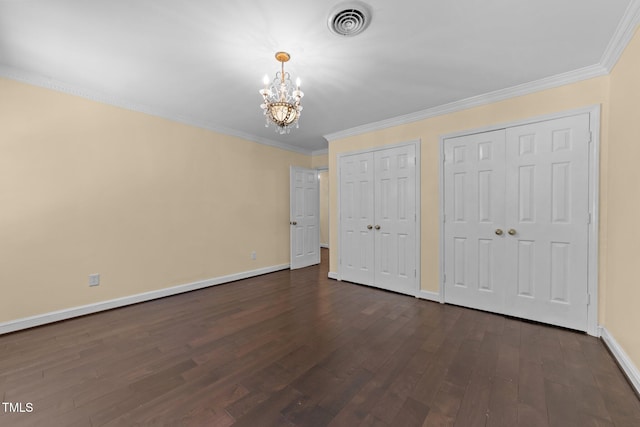 unfurnished bedroom featuring multiple closets, dark hardwood / wood-style floors, crown molding, and a notable chandelier