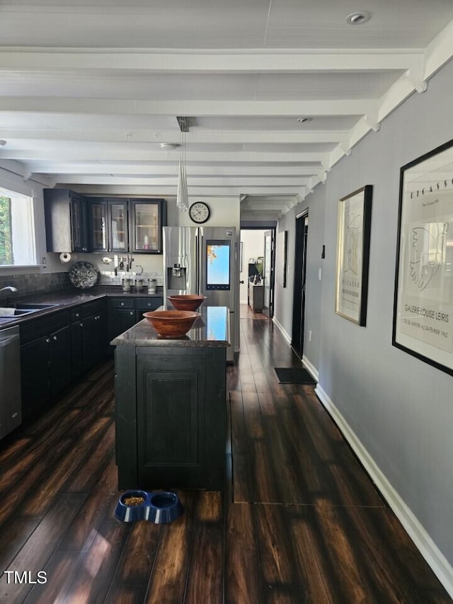 kitchen featuring dark countertops, beamed ceiling, glass insert cabinets, dark wood-type flooring, and a sink