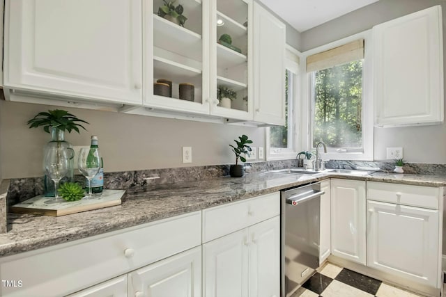 kitchen featuring white cabinets, stainless steel dishwasher, a sink, glass insert cabinets, and light stone countertops