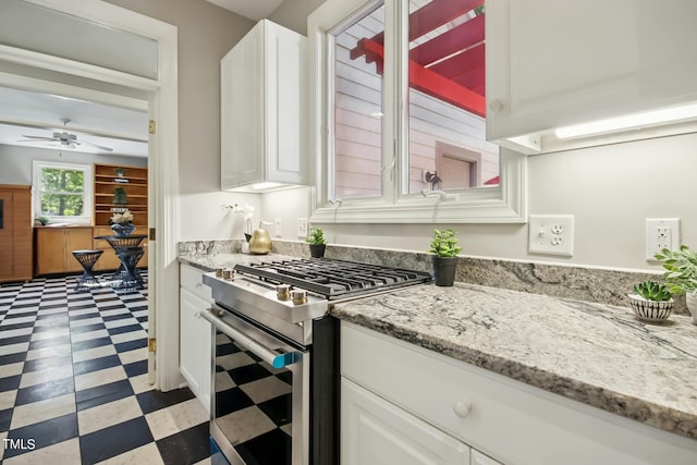 kitchen with stainless steel gas range oven, white cabinets, light stone counters, and ceiling fan